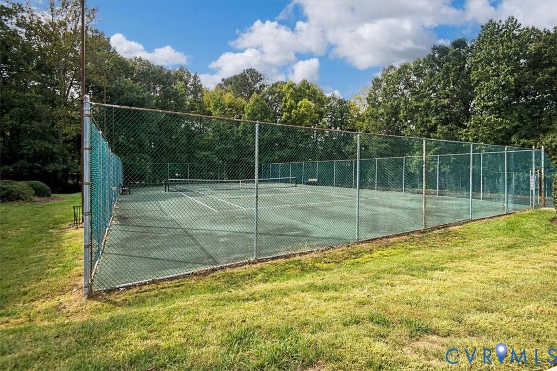 Outdoor tennis court featuring a fenced perimeter and surrounding mature trees