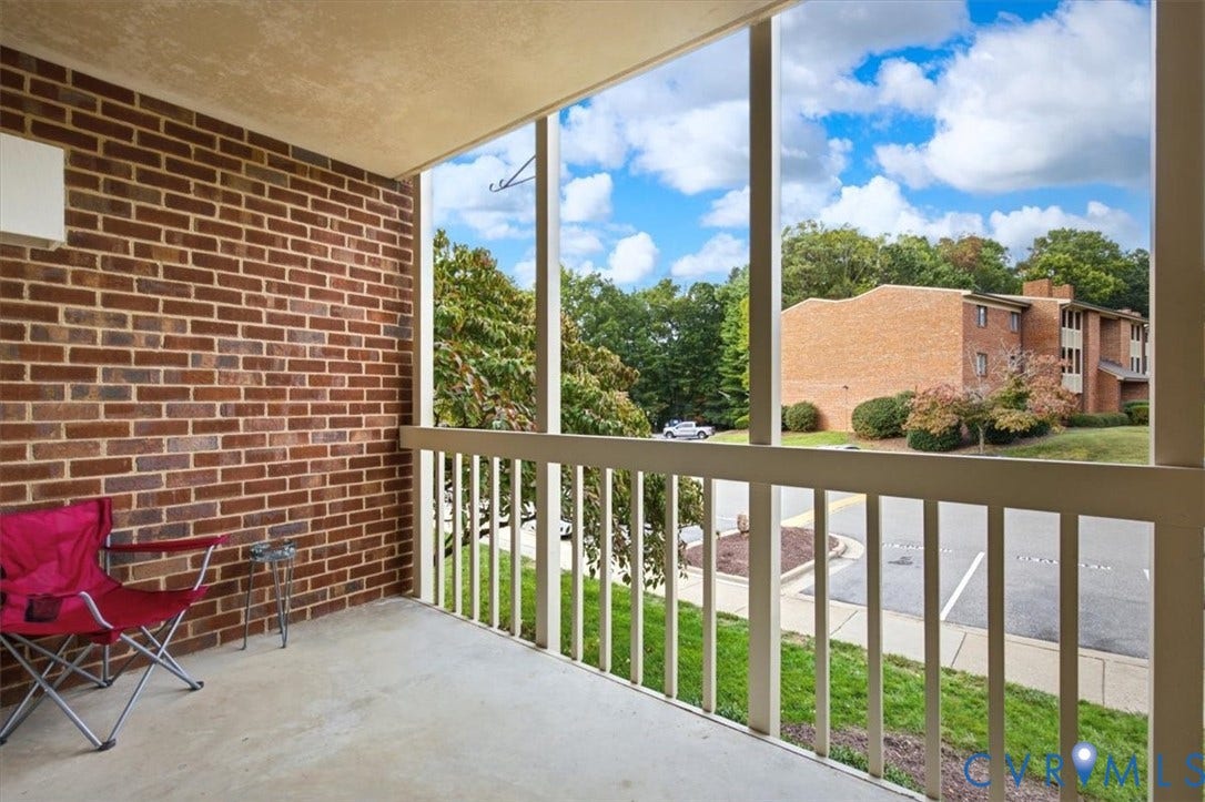 Covered exterior balcony featuring a brick accent wall, concrete flooring, and a protective railing