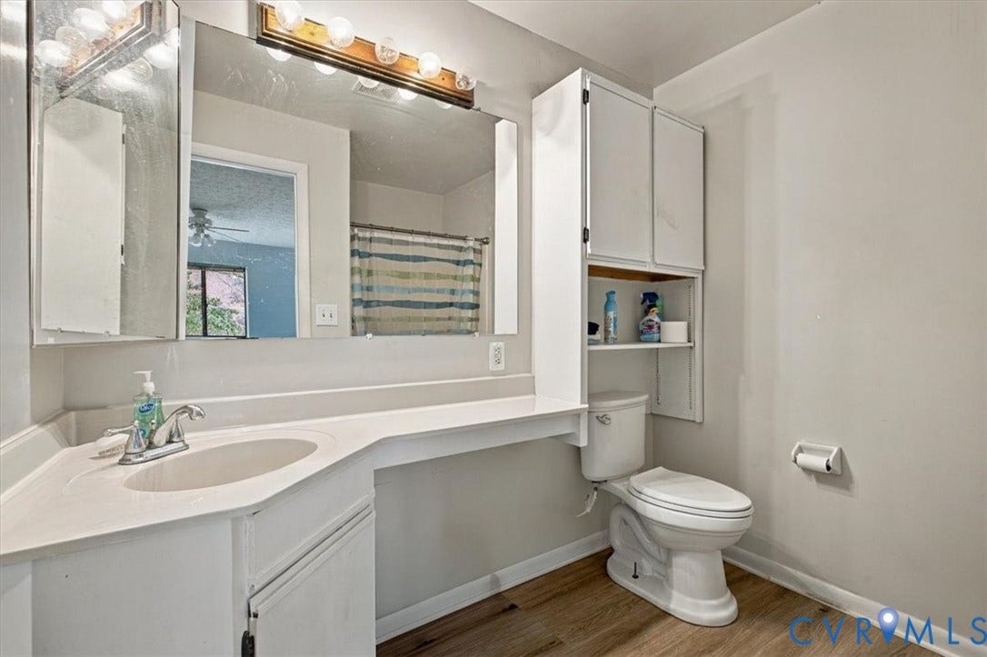 Bathroom featuring a large-format mirror, vanity with integrated sink, wood-finish flooring, and built-in vertical cabinetry