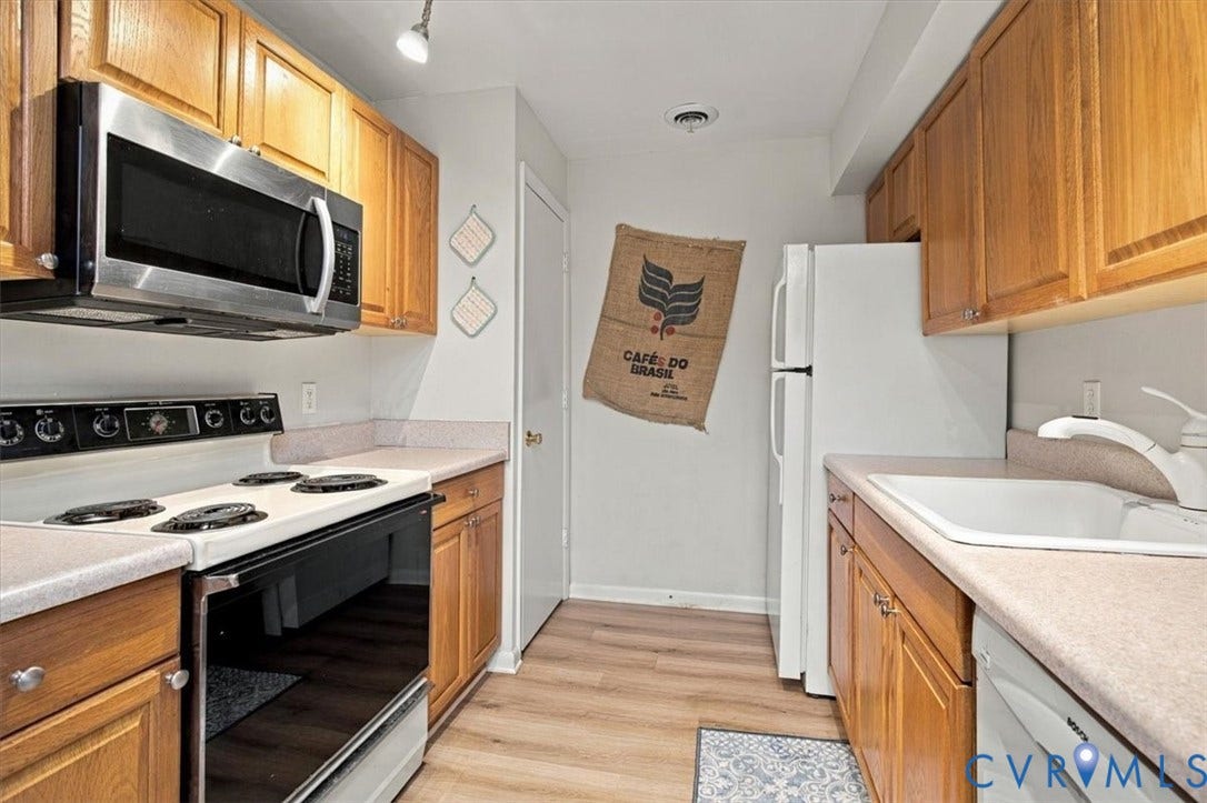 Galley kitchen featuring wood-finish cabinetry, stone-composite countertops, wood-finish flooring, and integrated stainless steel and white appliances