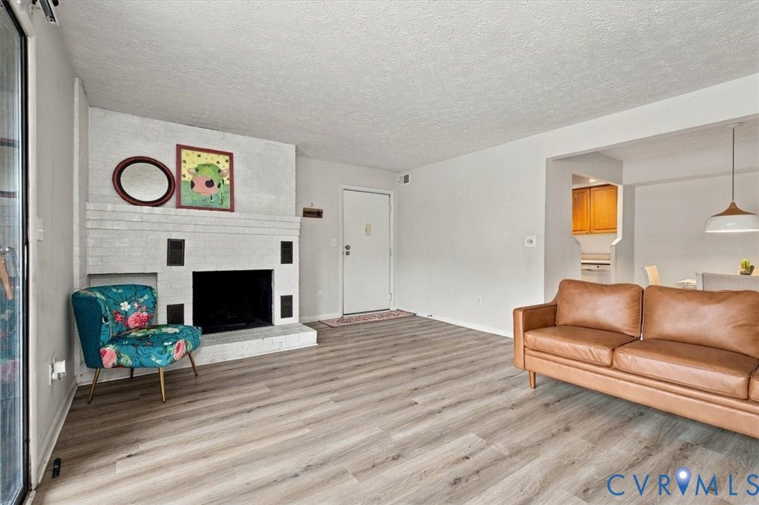 Living area featuring a floor-to-ceiling painted brick fireplace, wood-finish flooring, and a pendant light fixture
