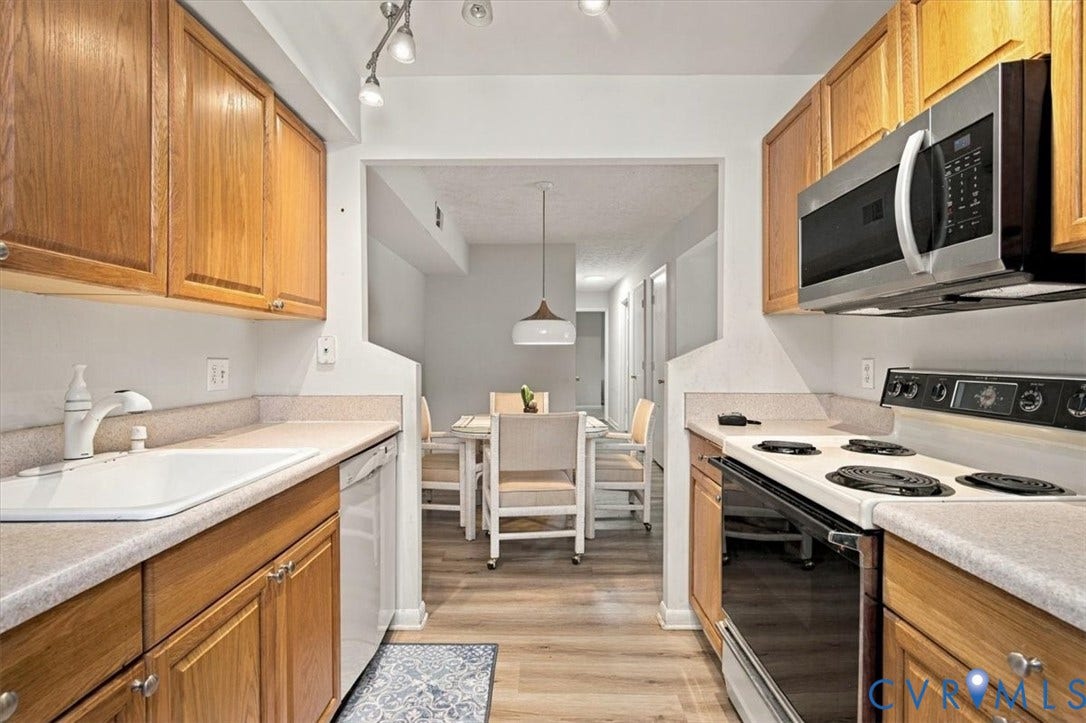 Kitchen featuring natural wood cabinetry, solid-surface countertops, integrated stainless steel appliances, and wood-finish flooring