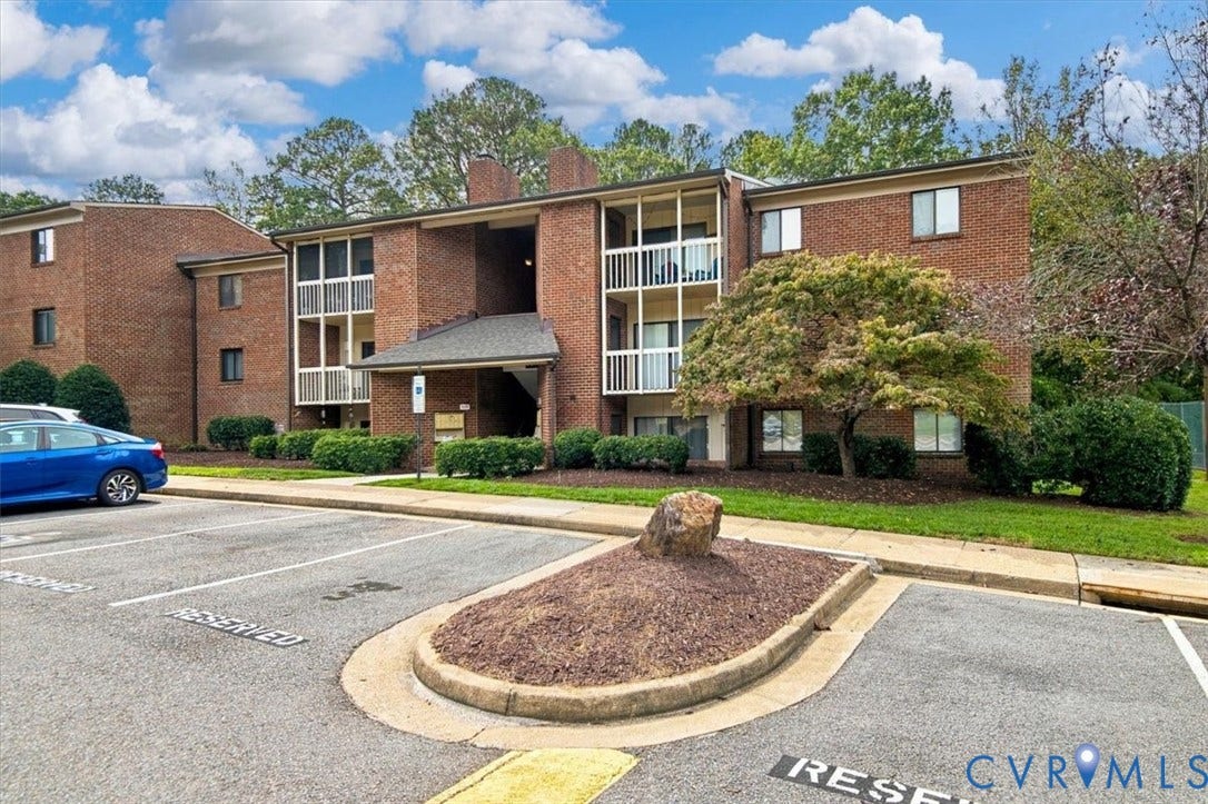 Multi-story brick exterior featuring screened balconies, shingled roofing, and paved parking area
