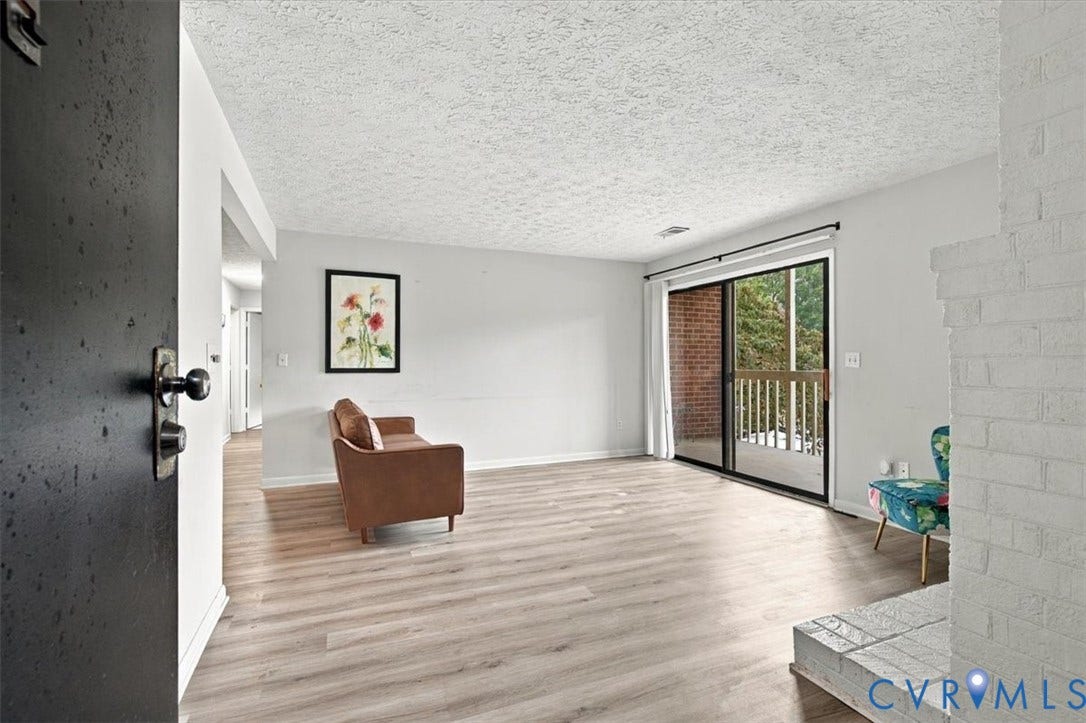 Wood-finish flooring, white-painted brick fireplace, and sliding glass door with external deck access