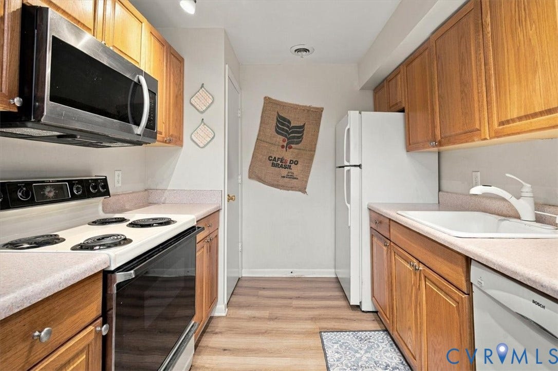 Kitchen featuring wood cabinetry, integrated stainless steel microwave, white range, white dishwasher, and wood-finish flooring
