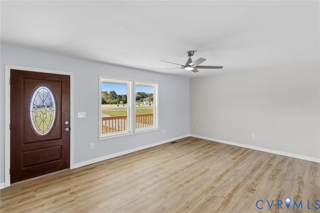79 Dixie Drive, Mathews, VA 23050 Wood-finish flooring, neutral wall tones, multi-pane entry door with oval decorative glass insert, dual windows with exterior rail visibility, and ceiling-mounted fan with integrated lighting