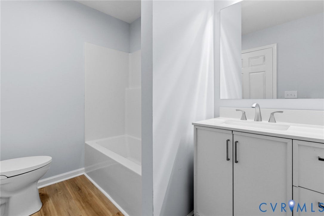 79 Dixie Drive, Mathews, VA 23050 Bathroom featuring a white vanity with matte black hardware, integrated sink, large wall-mounted mirror, wood-finish flooring, and a shower-tub combination with a white surround