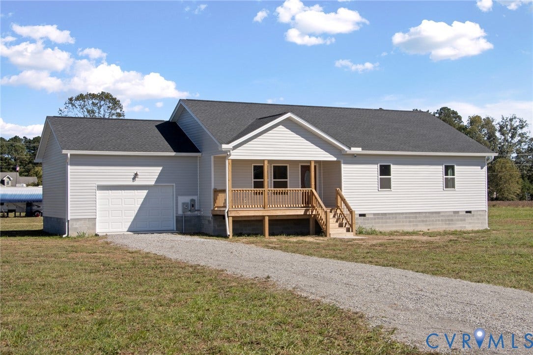 79 Dixie Drive, Mathews, VA 23050 Single-story residence featuring light-colored siding, a covered wooden front porch, an attached one-car garage, and a gravel driveway