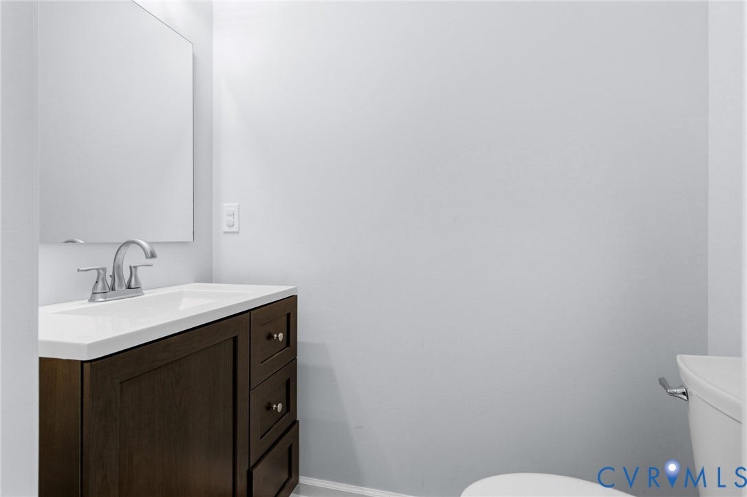 79 Dixie Drive, Mathews, VA 23050 Dark-finish wood cabinetry, integrated rectangular vanity sink, polished chrome dual-handle faucet, large wall-mounted mirror, and a white toilet