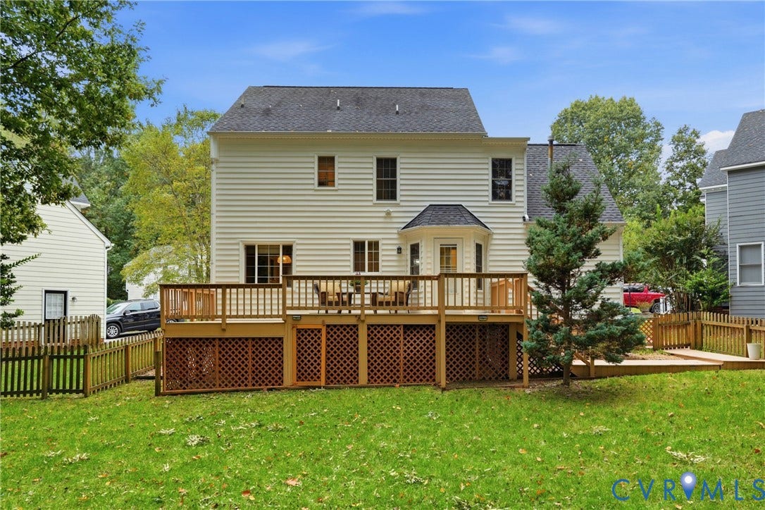 14800 Highberry Woods Drive, Midlothian, VA 23112 Rear elevation featuring light-colored horizontal siding, an elevated wood deck with lattice skirting, and a grassy backyard enclosed by wood fencing