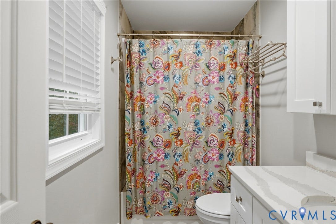 14800 Highberry Woods Drive, Midlothian, VA 23112 Bathroom featuring a white shaker-style vanity with a veined stone countertop, tub with neutral tiled surround, white horizontal blinds, and wall-mounted metal shelving