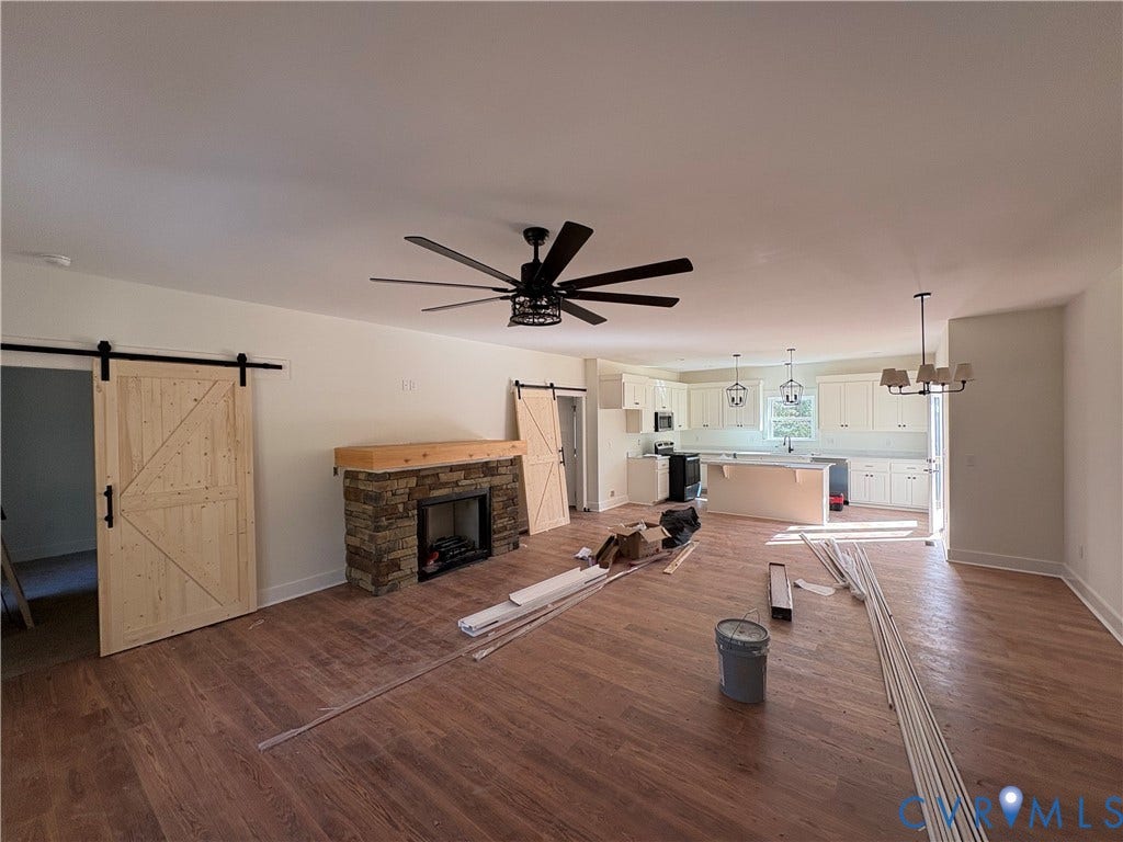15205 Lebanon Road, Parson's Retreat, Disputanta, VA 23842 Open-concept interior featuring wood-finish flooring, a stone fireplace with a natural wood mantel, two sliding barn doors, a multi-blade ceiling fan, and a kitchen island
