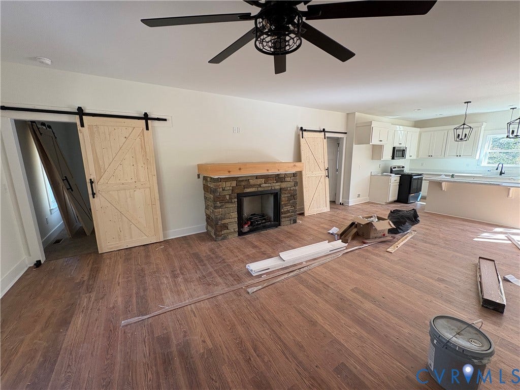 15205 Lebanon Road, Parson's Retreat, Disputanta, VA 23842 Open-concept space featuring wood-finish flooring, stone-veneer fireplace with a heavy timber mantel, dual natural-finish sliding barn doors, and white cabinetry
