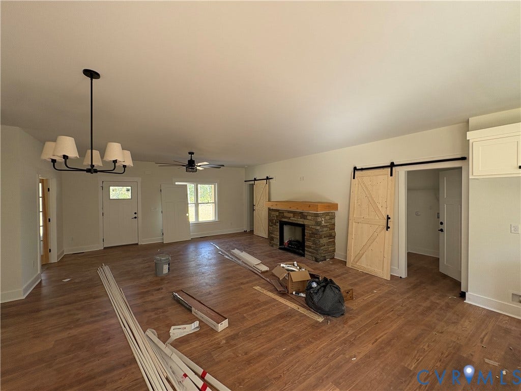 15205 Lebanon Road, Parson's Retreat, Disputanta, VA 23842 Living space featuring wood-finish flooring, a stone-faced fireplace with a natural wood mantel, sliding barn-style doors, and a multi-arm chandelier