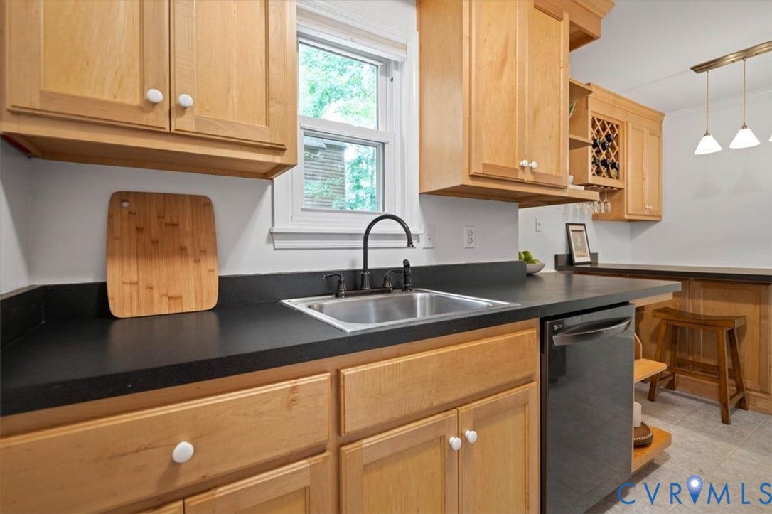 10209 Francill Court, North Chesterfield, VA 23236 Kitchen featuring light-tone wood cabinetry, solid-surface countertops, built-in wine rack, integrated stainless steel sink with matte black faucet, and pendant lighting