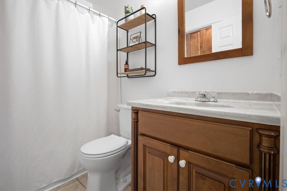 10209 Francill Court, North Chesterfield, VA 23236 Bathroom vanity featuring a wood finish, neutral countertop with an integrated sink, metal-framed wall shelving, and a wood-framed wall mirror