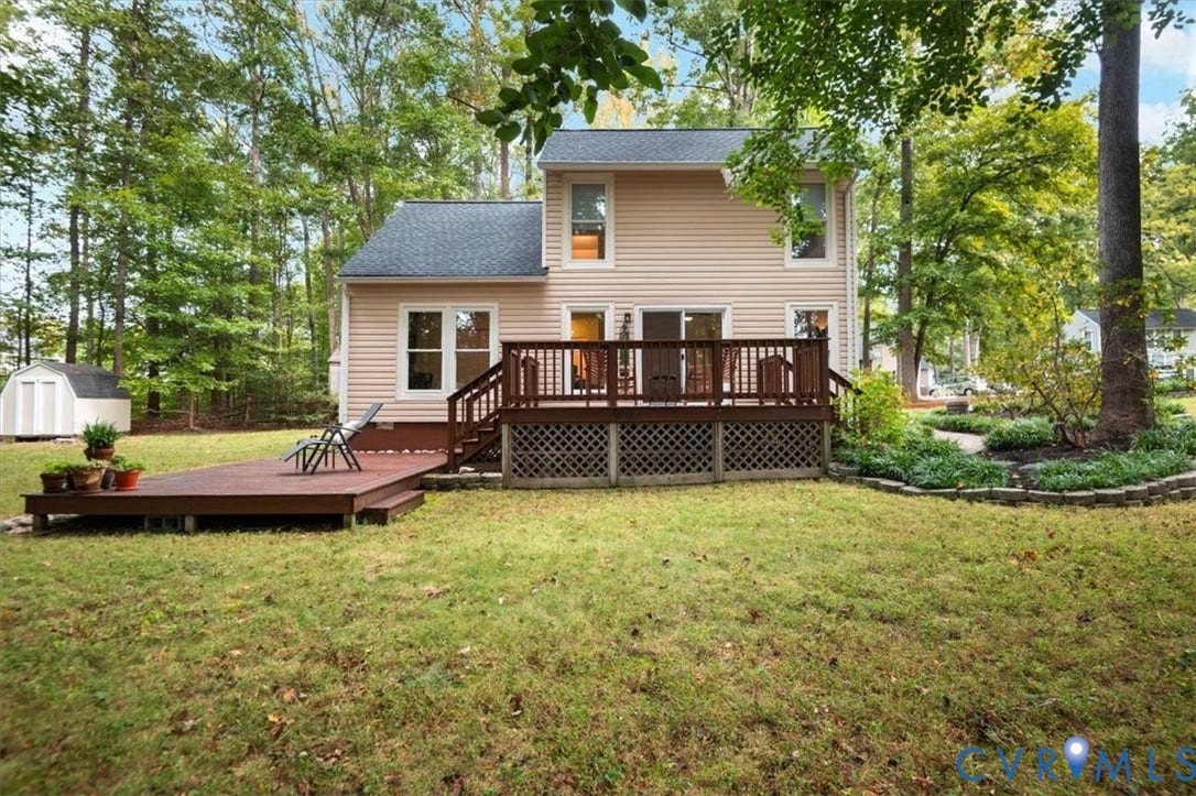 10209 Francill Court, North Chesterfield, VA 23236 Two-story residence featuring light-toned vinyl siding, a multi-level wood deck, lattice skirting, and a detached storage shed situated on a wooded lot