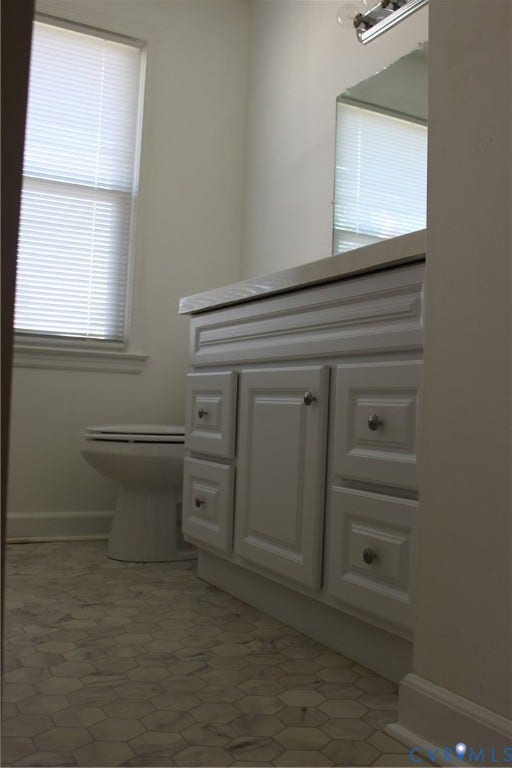 905 Williamsburg Road, Colonial Heights, VA 23834 White vanity with raised-panel cabinetry, neutral stone countertop, geometric tile flooring, and wall-mounted vanity lighting