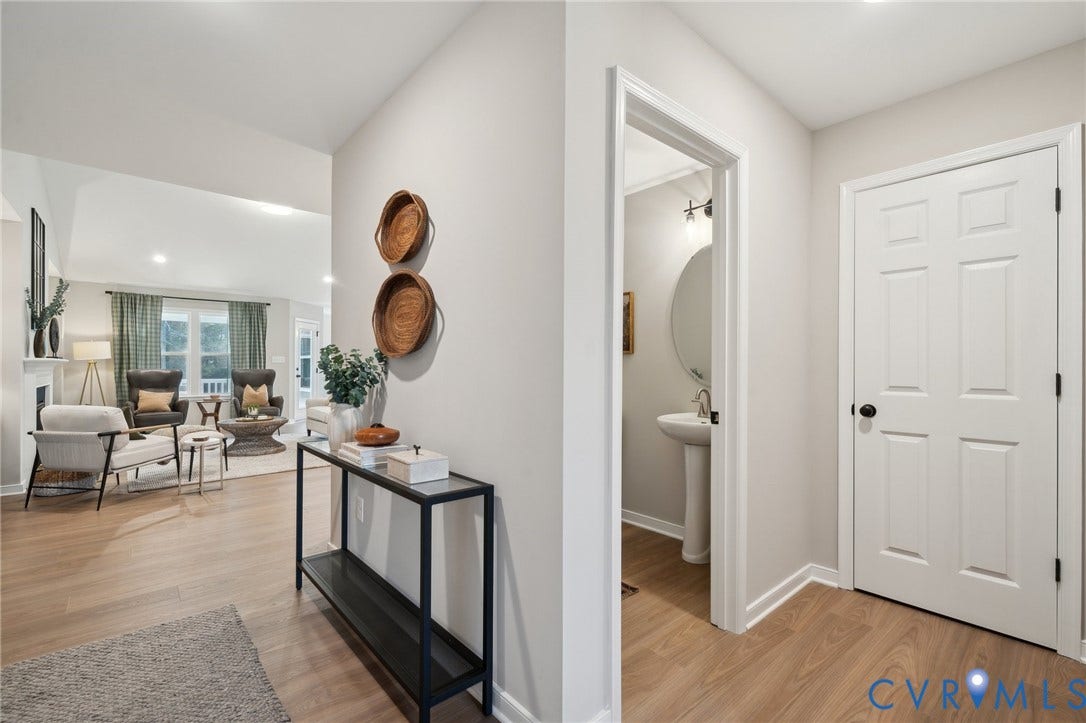 Entryway featuring wood-finish flooring, six-panel interior door with matte black hardware, and an auxiliary room containing a pedestal sink and circular wall-mounted mirror