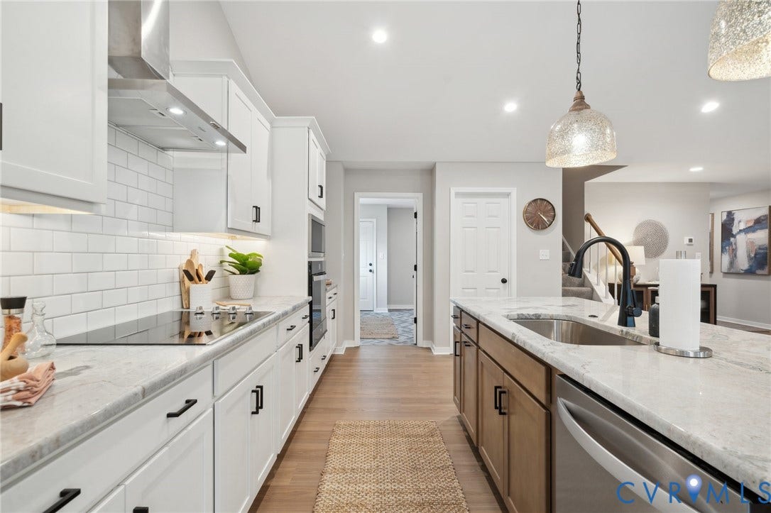 Kitchen featuring white cabinetry with matte black hardware, stone-finish countertops, subway tile backsplash, stainless steel appliances, and wood-finish flooring
