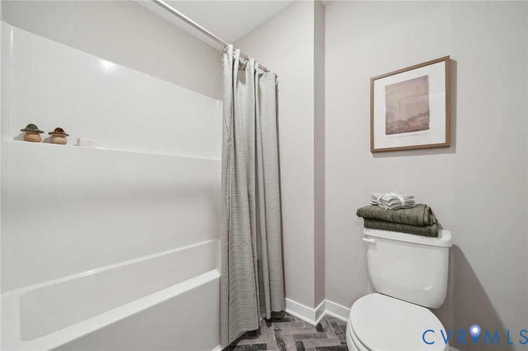 Bathroom featuring a white composite tub and shower surround, a porcelain toilet, and herringbone-patterned tile flooring