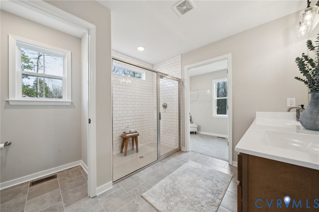 Bathroom featuring a dual-sink vanity with white countertops, a glass-enclosed shower with subway tile surround, and large-format tile flooring