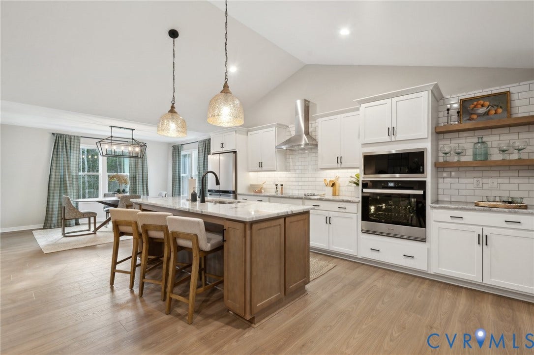 Kitchen featuring white shaker cabinetry, a contrasting wood-tone central island, stone countertops, subway tile backsplash, and stainless steel built-in appliances including a wall oven and chimney-style range hood