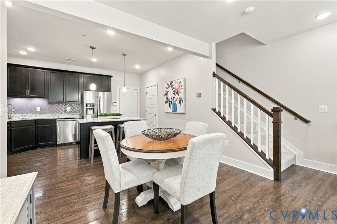 4223 Saunders Tavern Trail, #A, Henrico, VA 23233 Kitchen featuring dark cabinetry, stone countertops, stainless steel appliances, and a herringbone-patterned backsplash, complemented by wood-finish flooring and a staircase with white spindles and a stained-wood handrail