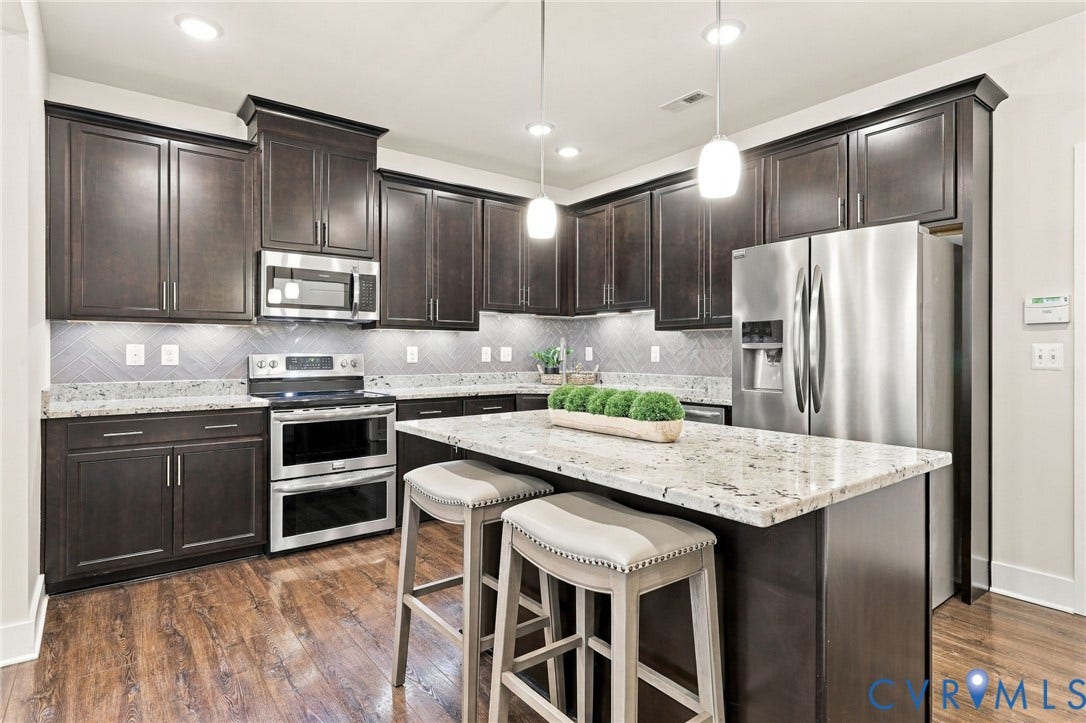 4223 Saunders Tavern Trail, #A, Henrico, VA 23233 Kitchen featuring dark wood cabinetry, stone countertops, stainless steel appliances, herringbone-patterned tile backsplash, and a central island with integrated seating