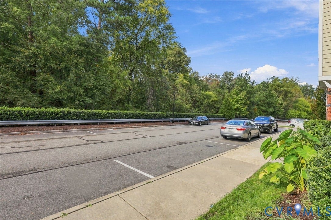 4223 Saunders Tavern Trail, #A, Henrico, VA 23233 Asphalt parking area with designated stalls, concrete sidewalk, mature perimeter greenery, and metal guardrail