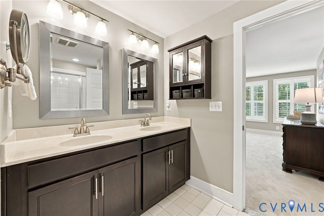 4223 Saunders Tavern Trail, #A, Henrico, VA 23233 Dual-sink vanity with dark cabinetry and stone countertop, two framed mirrors, wall-mounted light fixtures, and wall-mounted storage cabinetry