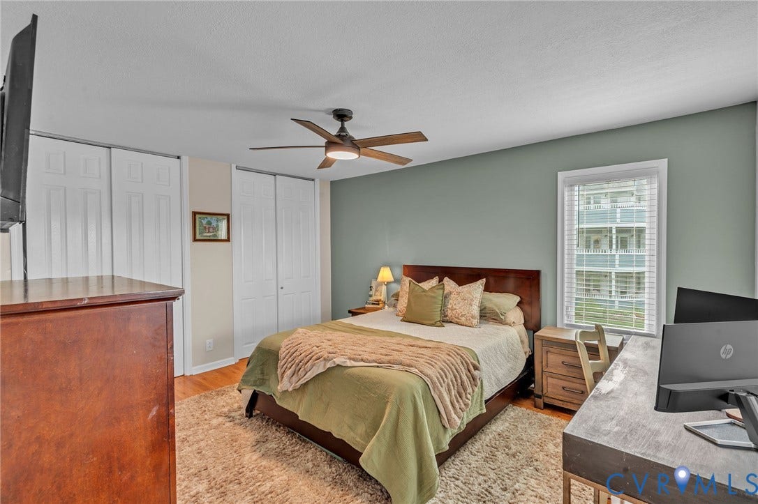 Bedroom interior featuring a dark-finish ceiling fan, wood-finish flooring, dual-panel closet doors, and an accent wall