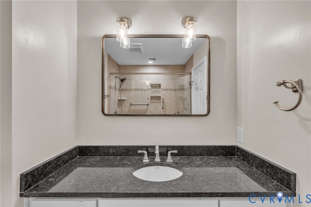 Bathroom vanity featuring a stone countertop with an integrated basin, dual-light wall fixture, framed rectangular mirror, and brushed-finish hardware