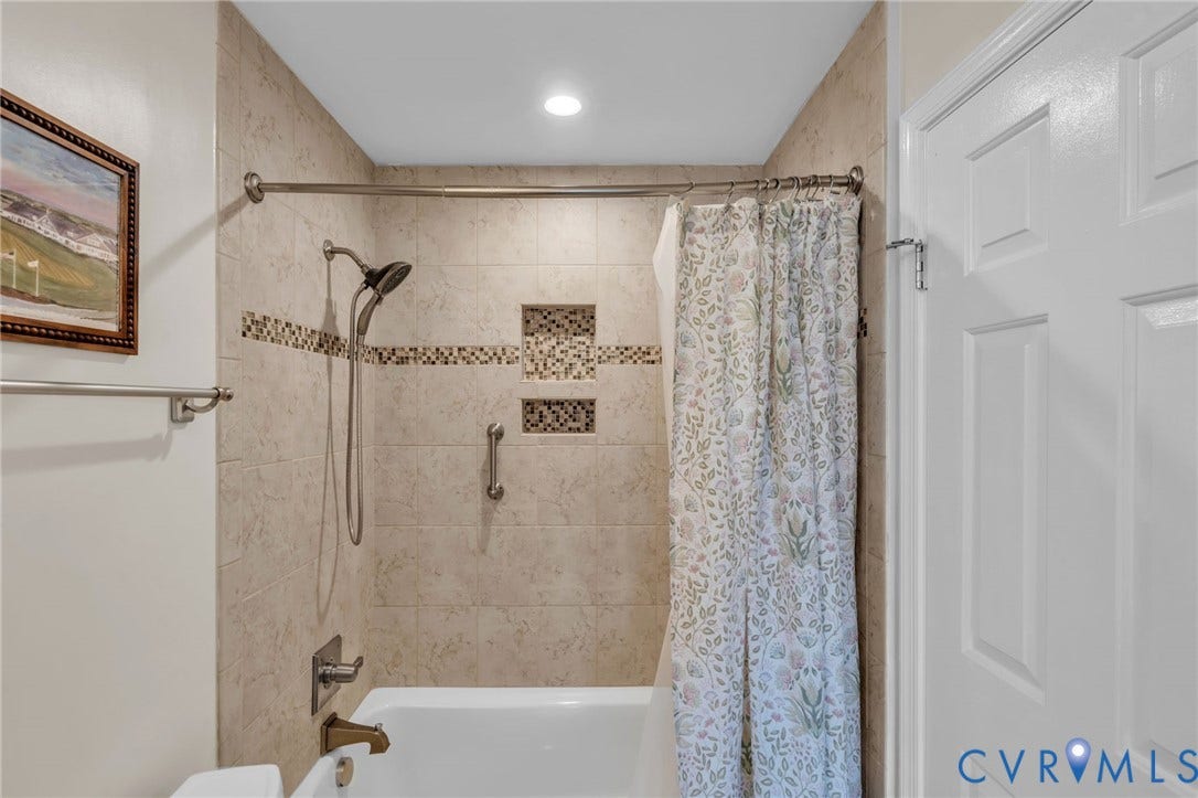 Tiled shower enclosure featuring a multi-function shower head, mosaic accent tiling, recessed shelving, and a metal grab bar