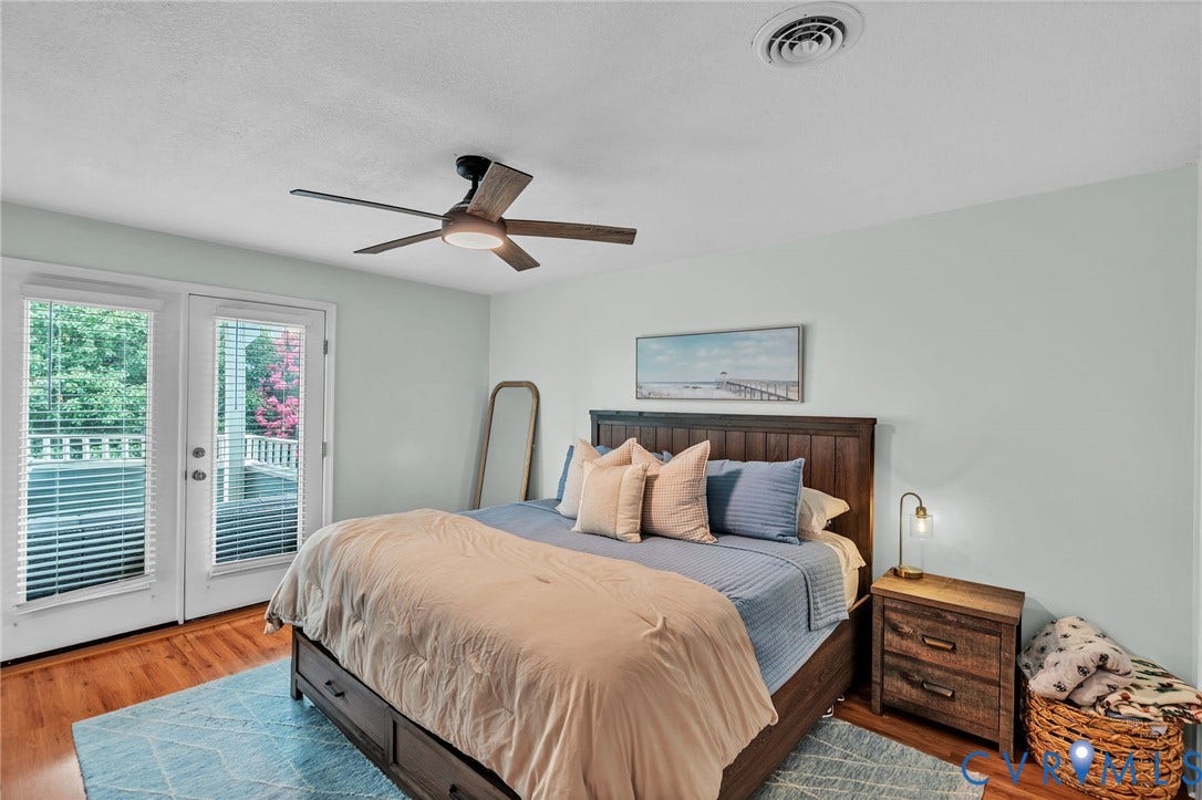 Bedroom featuring wood-finish flooring, a central ceiling fan with integrated lighting, and full-glass exterior doors providing access to an outdoor area