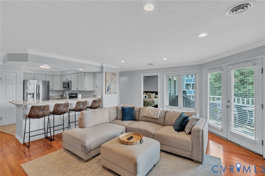 Open-concept living space featuring wood-finish flooring, recessed lighting, crown molding, a breakfast bar with stone-surface countertop, and glass-paneled patio doors
