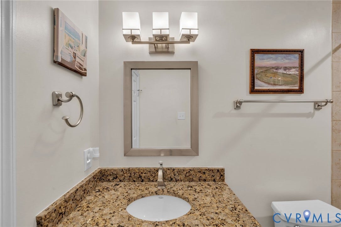 Stone countertop with an integrated basin, three-light brushed-nickel vanity fixture, framed wall mirror, and coordinating brushed-nickel towel hardware
