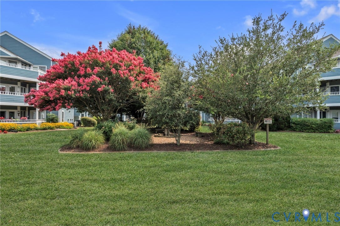 Landscaped common area featuring a manicured lawn, mature flowering trees, ornamental shrubs, and mulch-bed plantings