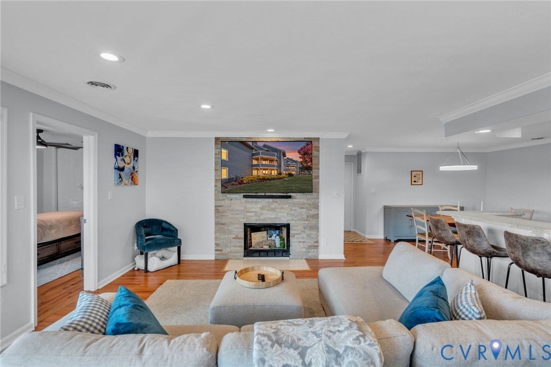 Living area featuring a floor-to-ceiling stone-veneer fireplace surround, wood-finish flooring, recessed lighting, and crown molding