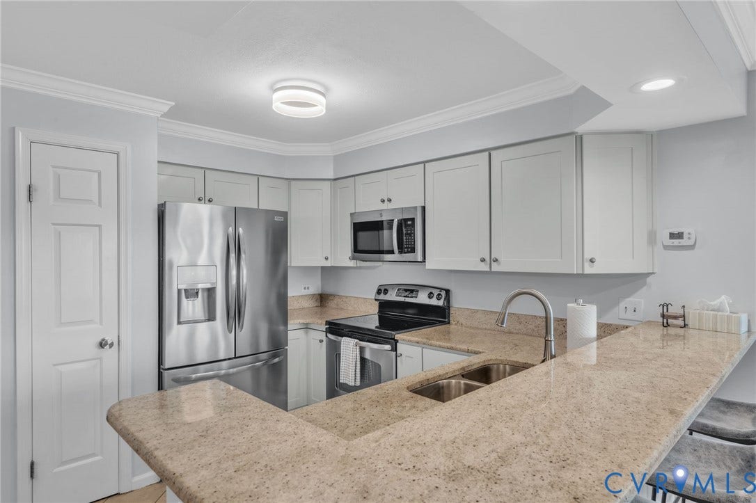 Kitchen featuring light-toned cabinetry, stone-surface countertops, stainless steel refrigerator and range, built-in microwave, and an integrated breakfast bar