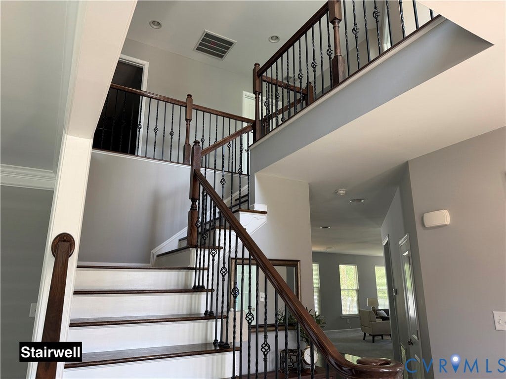 Staircase featuring wood-finish treads and handrails with decorative black metal balusters and a double-height ceiling