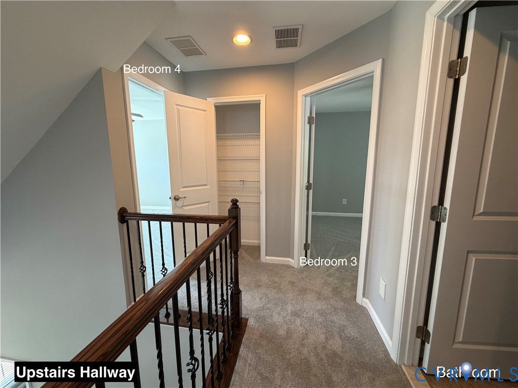 Hallway featuring a stained wood handrail, metal balusters, neutral carpeting, and interior doors with molded panel detailing