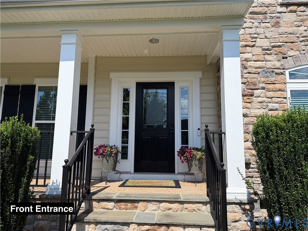 Covered front porch featuring stacked stone siding, square support columns, black metal railings, and a front door with glass sidelights