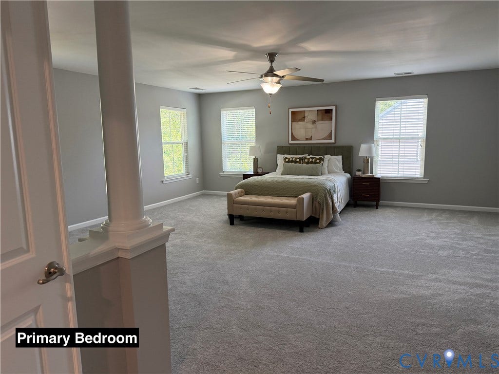 Spacious room featuring neutral carpeting, triple-window natural light exposure, a central ceiling fan with an integrated light fixture, and a decorative column with a half-wall partition