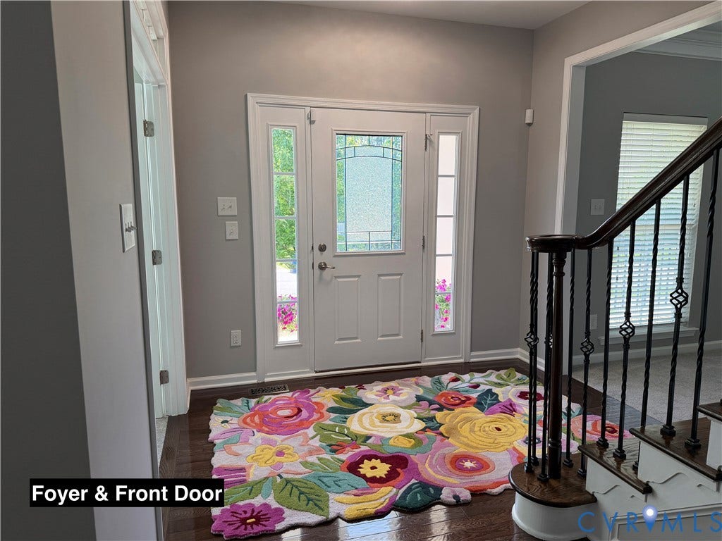 Foyer featuring a front door with decorative glass inserts and sidelights, wood-finish flooring, and a staircase with ornate metal balusters and a dark wood handrail