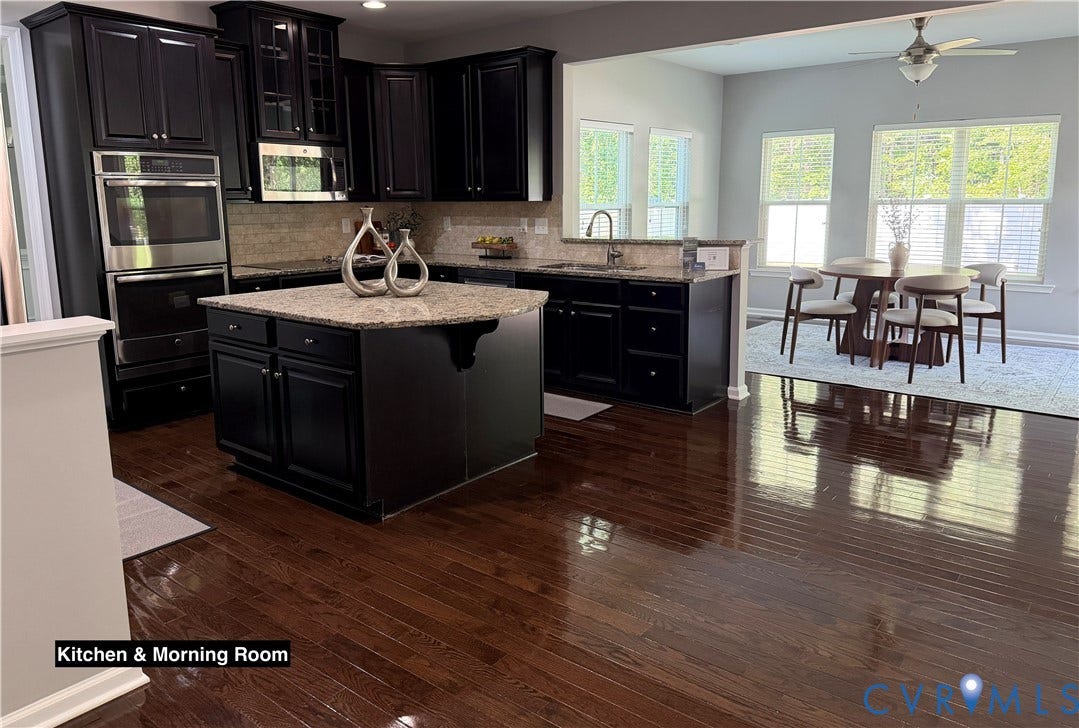 Kitchen featuring dark cabinetry, stone countertops, a center island, built-in double wall ovens, and wood-finish flooring