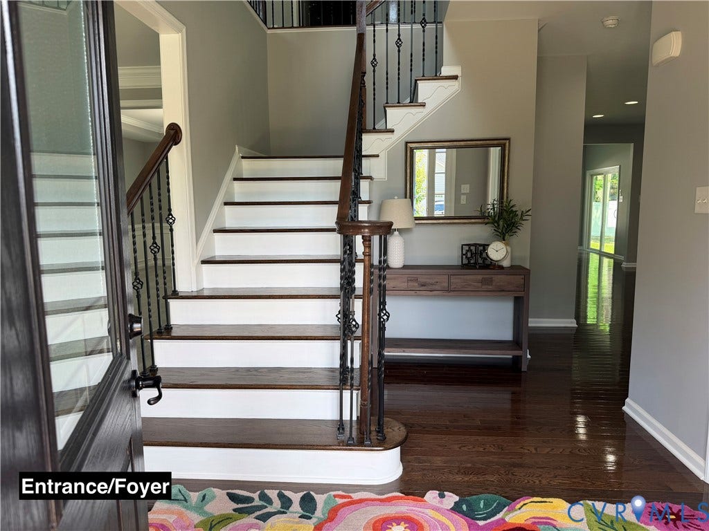 Foyer featuring dark wood-finish flooring, a staircase with white risers and dark wood-finish treads, and decorative wrought iron balusters with a polished wood handrail