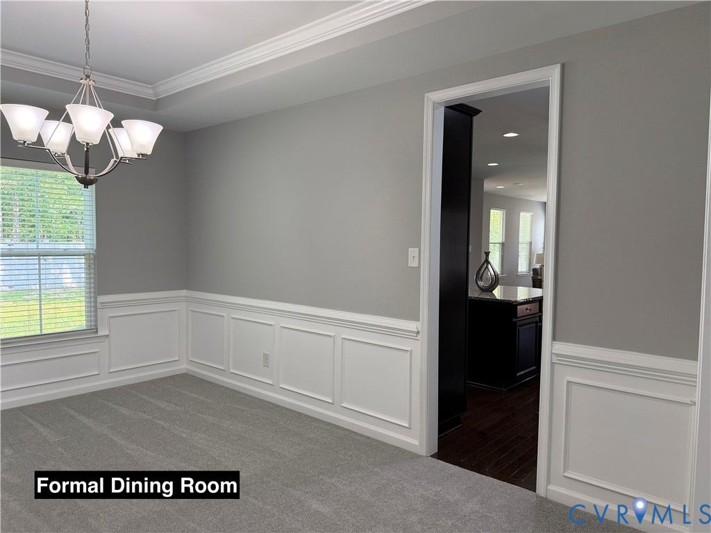 Dining room featuring crown molding, decorative wainscoting, wall-to-wall carpeting, and a multi-arm chandelier