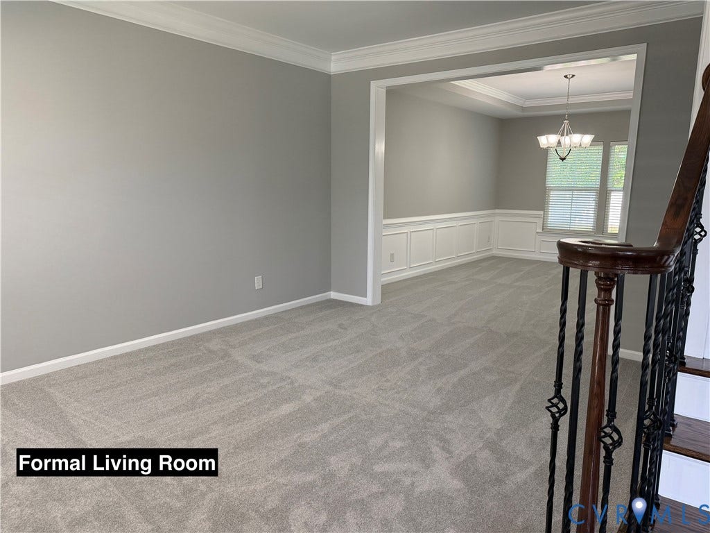 Interior space featuring decorative crown molding, wainscoting, a tiered ceiling, and a staircase with a wood handrail and iron balusters