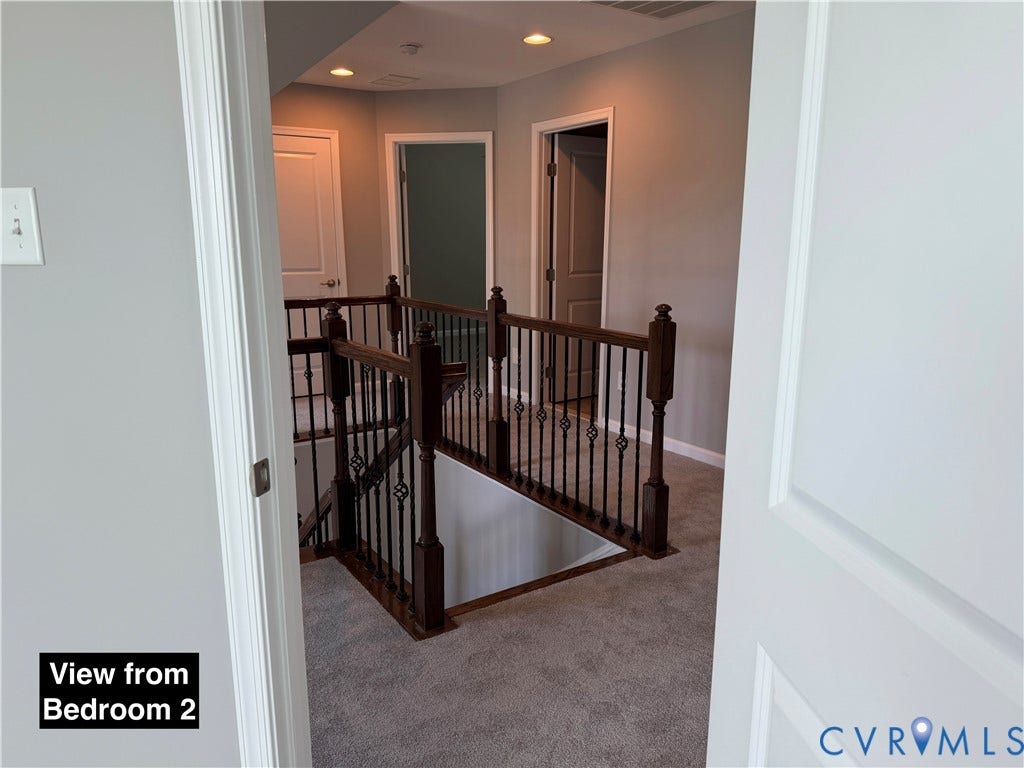 Hallway featuring dark wood-finish newel posts, iron balusters, recessed lighting, and neutral carpeting